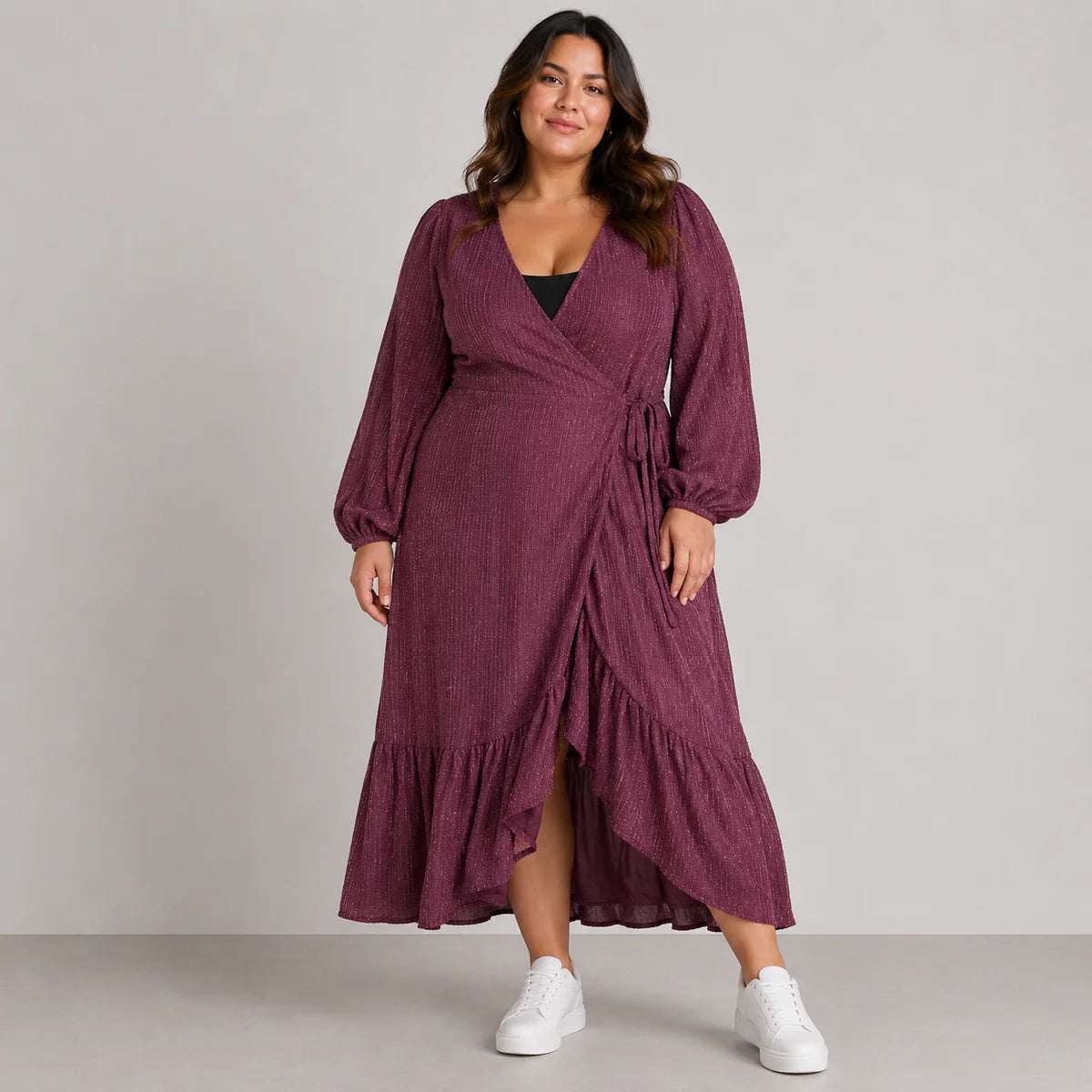 Woman wearing a purple wrap dress with white sneakers on a plain background