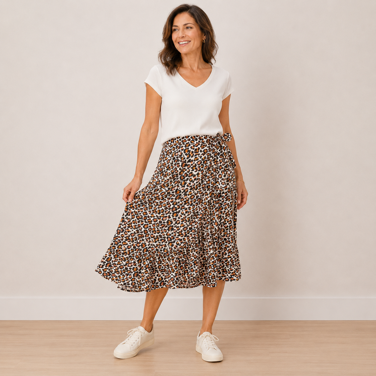 A woman modeling a white short-sleeve V-neck top and a brown leopard-print midi skirt with white sneakers, standing against a plain beige wall.