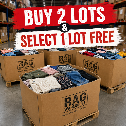 Three large cardboard boxes of folded clothing on pallets in a warehouse setting, with a bold promotional text overlay reading 'BUY 2 LOTS & SELECT 1 LOT FREE'. The boxes are branded 'RAG WAREHOUSE'.